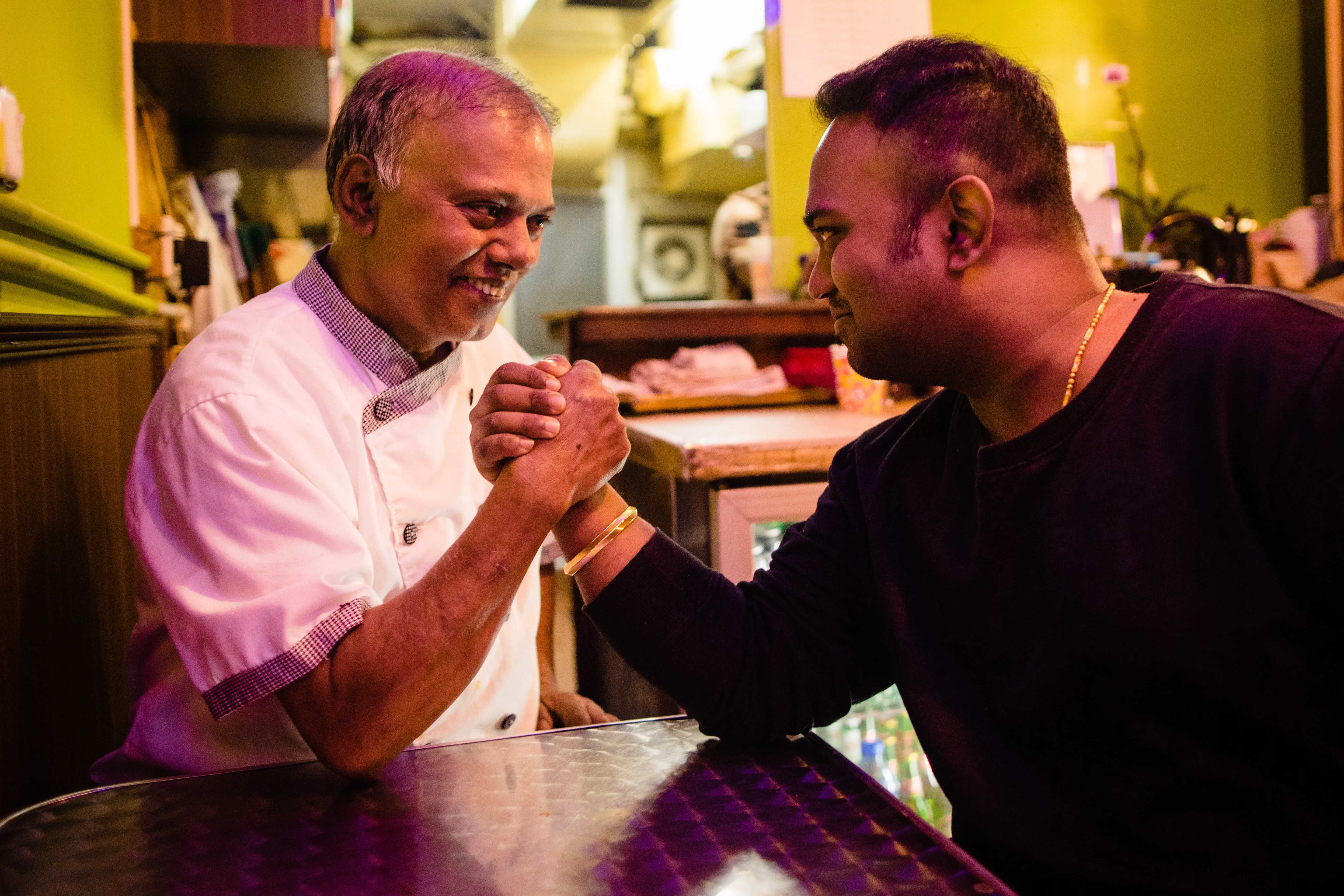 Monu Gomes and Alex Gomes at a table in the restaurant, hands clasped, both laughing