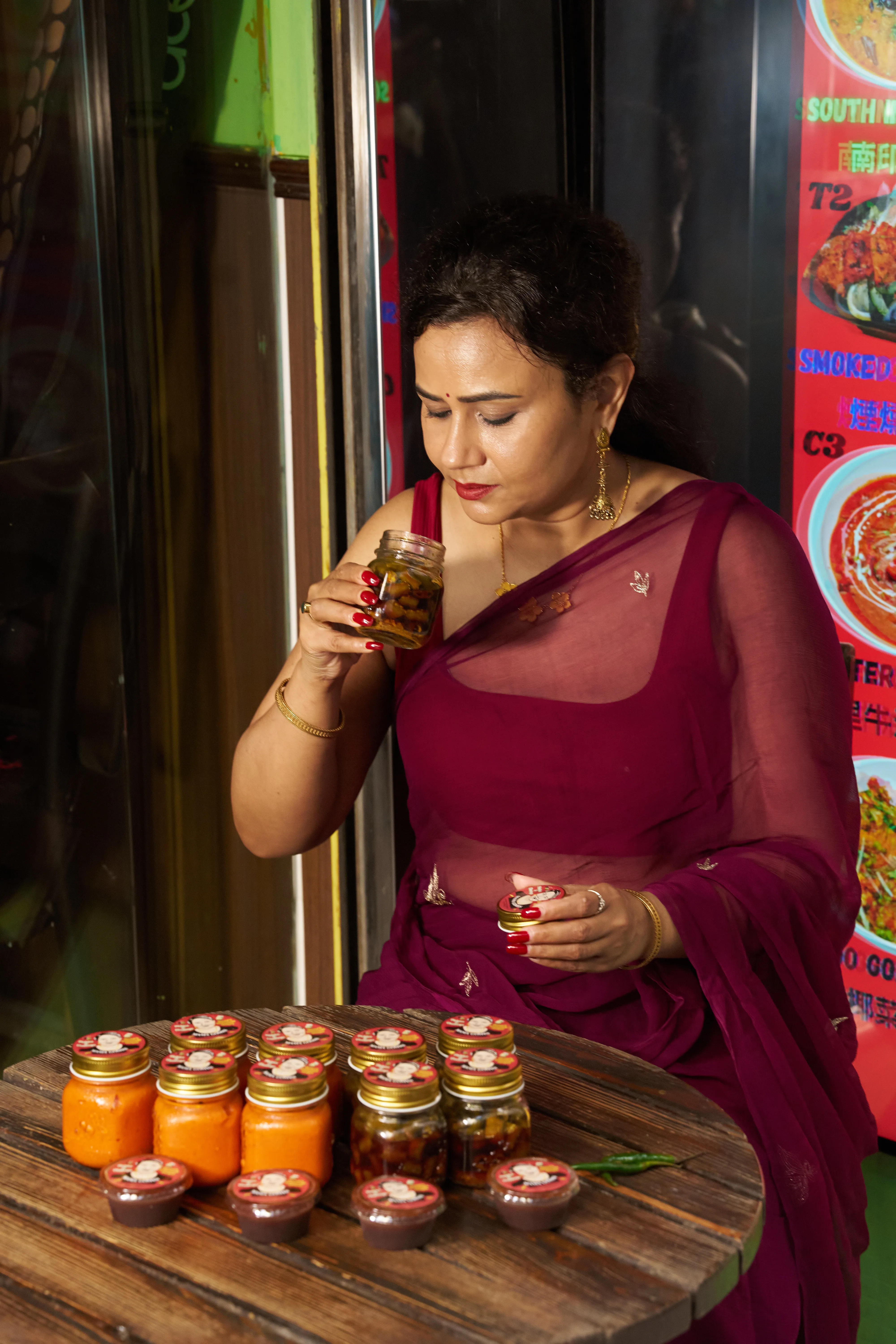 Mama Gomes in a plum sari, eyes closed, smelling an open jar of her pickle